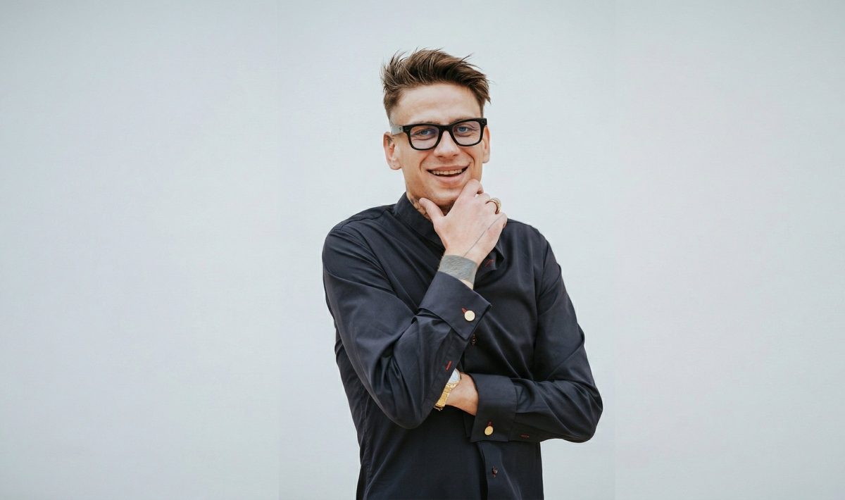 André Kohout s rukou u brady, v černé košili na světlém pozadí